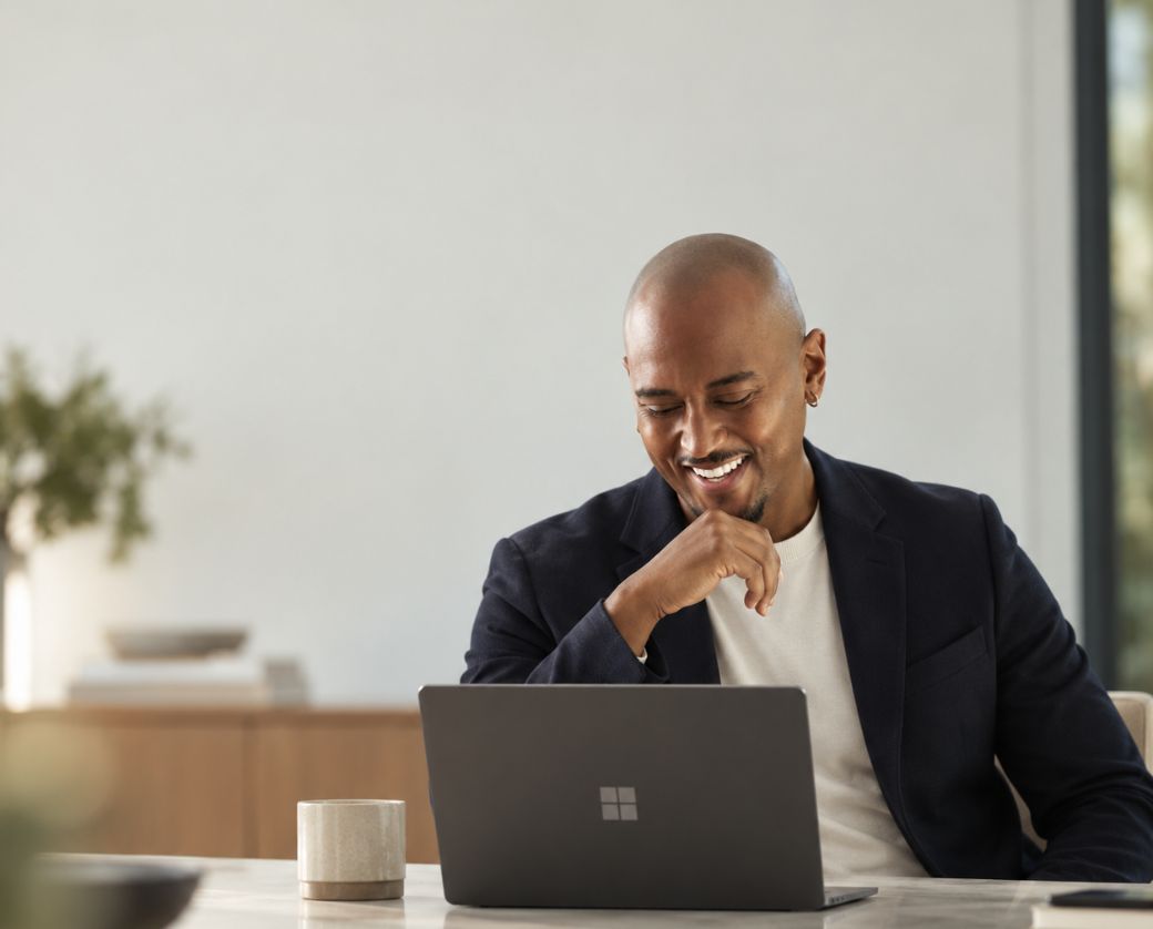 A smiling IT professional working at a laptop in a bright office