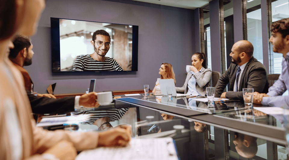 Employees watching a live town hall on a large screen in a conference room, connected via video call