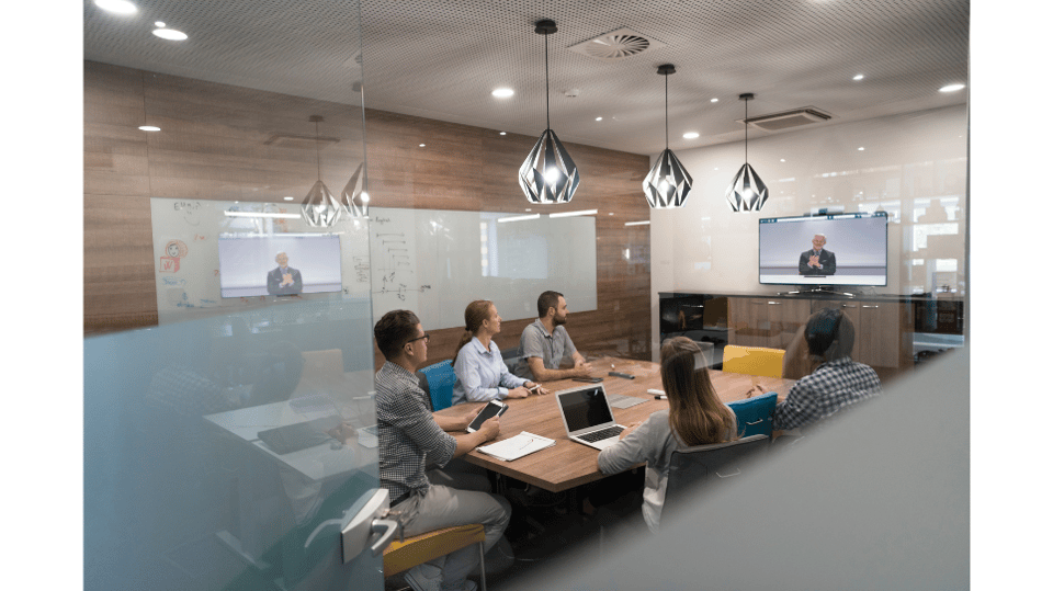 Hybrid meeting room with in-person team connected to remote speaker via video call on large screen