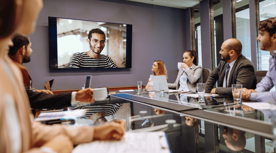 Employees watching a live town hall on a large screen in a conference room, connected via video call